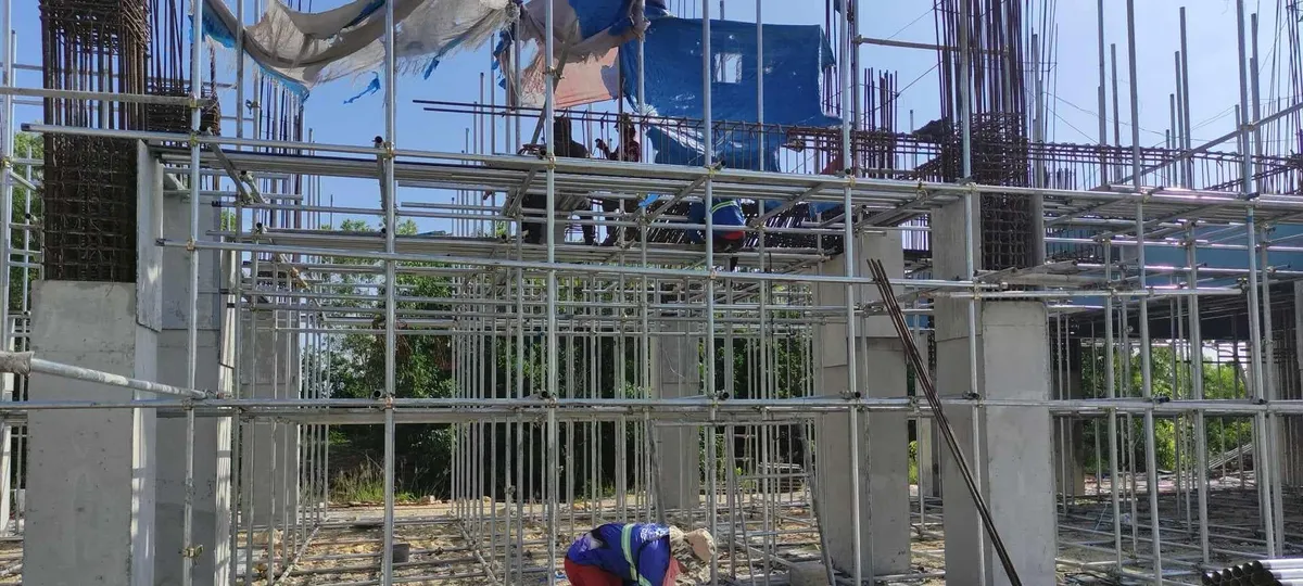 Scaffolding and cast concrete columns rising at the Cebu Technological University multi-purpose building in Borbon, with a worker setting out reinforcing bar at ground level.