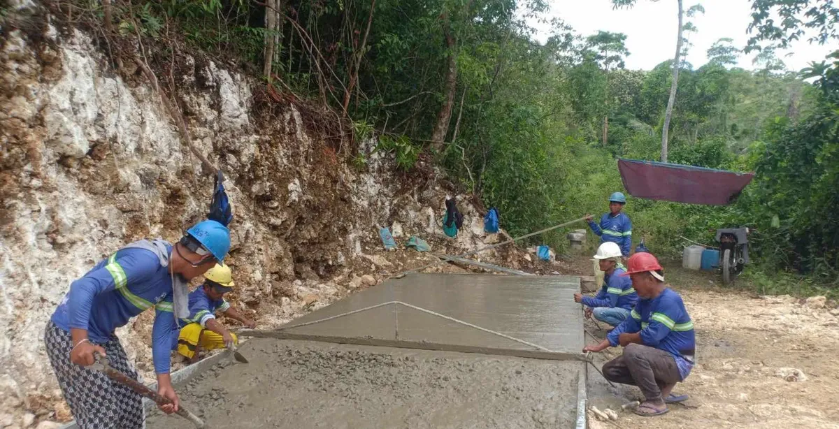 A crew screeding and finishing a freshly poured concrete road in Barangay Bingay, Borbon, cut into a limestone hillside.